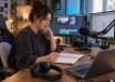 Digital creator reviewing a budget notebook beside a laptop, monitors and streaming equipment.