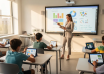 Teacher using an interactive classroom display while students work on tablets