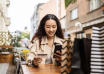 Woman holding a bank card and smartphone at an outdoor café table.