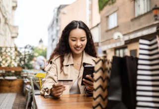 Woman holding a bank card and smartphone at an outdoor café table.