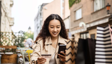 Woman holding a bank card and smartphone at an outdoor café table.