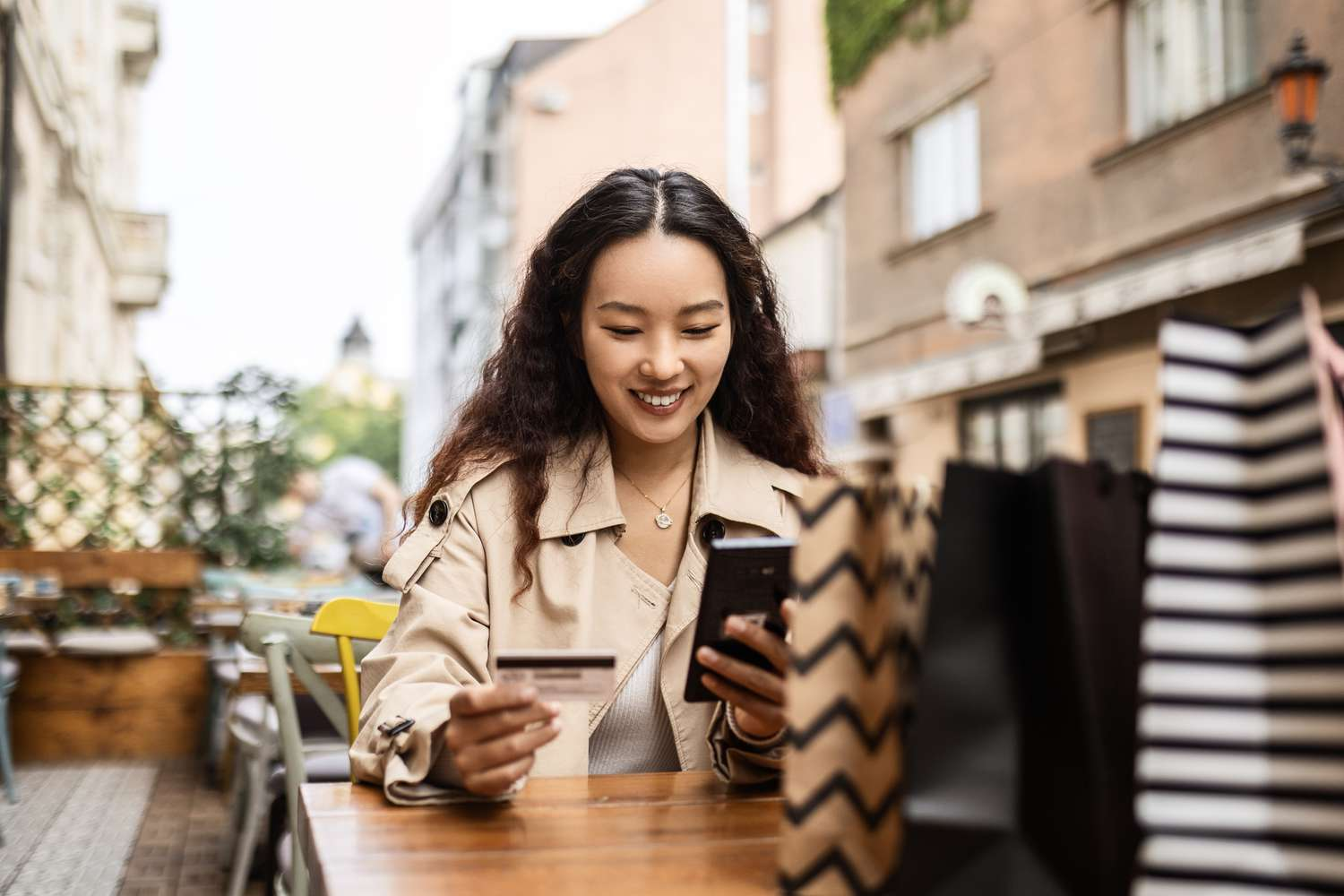 Woman holding a bank card and smartphone at an outdoor café table.