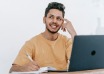 Man considering an idea while writing in a notebook beside his laptop