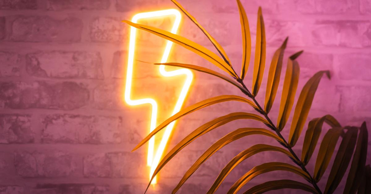 Yellow lightning-bolt LED neon sign beside a plant on a pink-lit wall