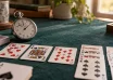 Playing cards on green felt beside an analogue stopwatch