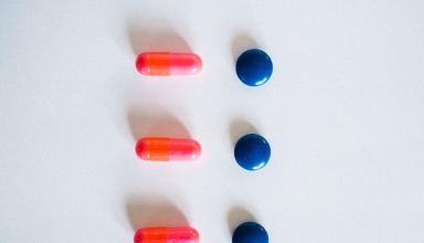 Pink capsules and round blue tablets arranged on a white background
