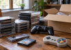 Retro video game cartridges, disc cases and controllers beside an open shipping box.