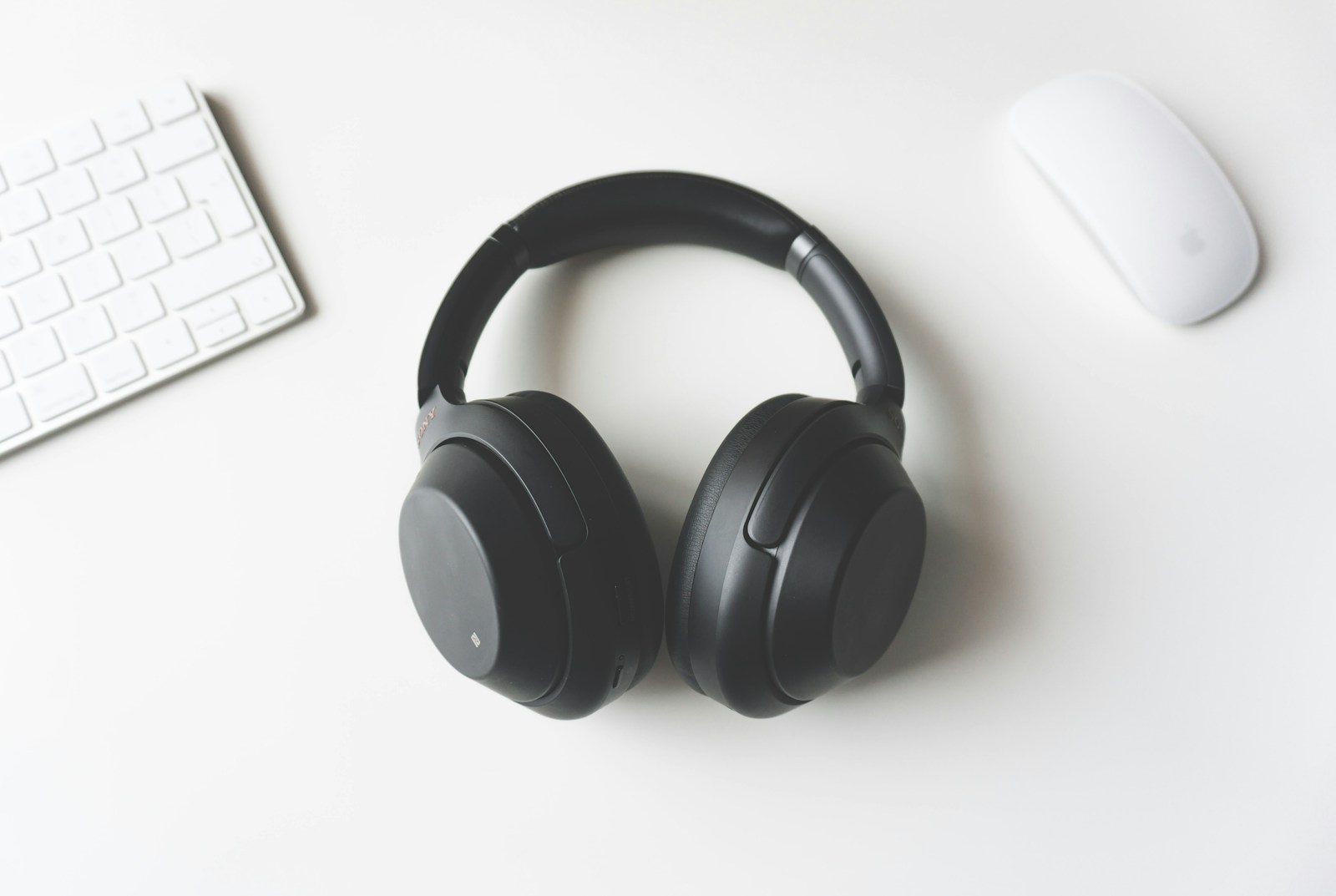Black over-ear headphones on a white desk beside a keyboard and mouse.