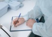 A doctor in protective clothing writes medical notes on a clipboard