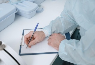 A doctor in protective clothing writes medical notes on a clipboard