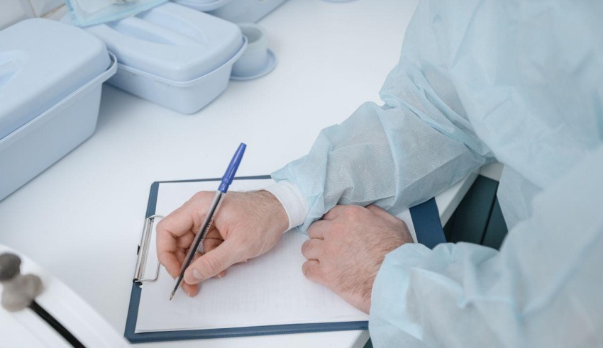 A doctor in protective clothing writes medical notes on a clipboard