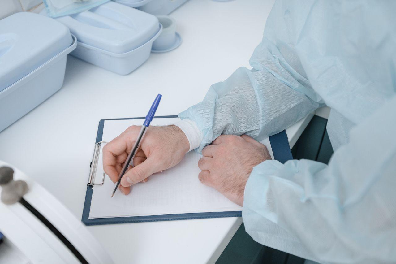 A doctor in protective clothing writes medical notes on a clipboard