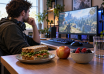 A gamer at a PC desk with a sandwich, fruit and a glass of water ready for a meal break.